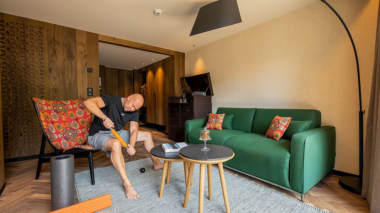 Homme utilisant un appareil de massage dans un salon moderne, entouré de meubles et d'équipements sportifs.
