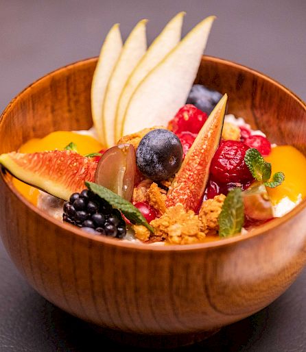 Bol en bois rempli de fruits frais, granola et yaourt. Servi sur un fond sombre.