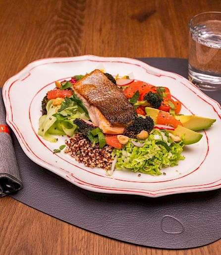 Une assiette avec du poisson grillé, des légumes et du quinoa sur une table en bois, à côté d'un verre d'eau.