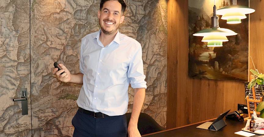 A man in a shirt stands smiling in an office with an antique map on the wall.