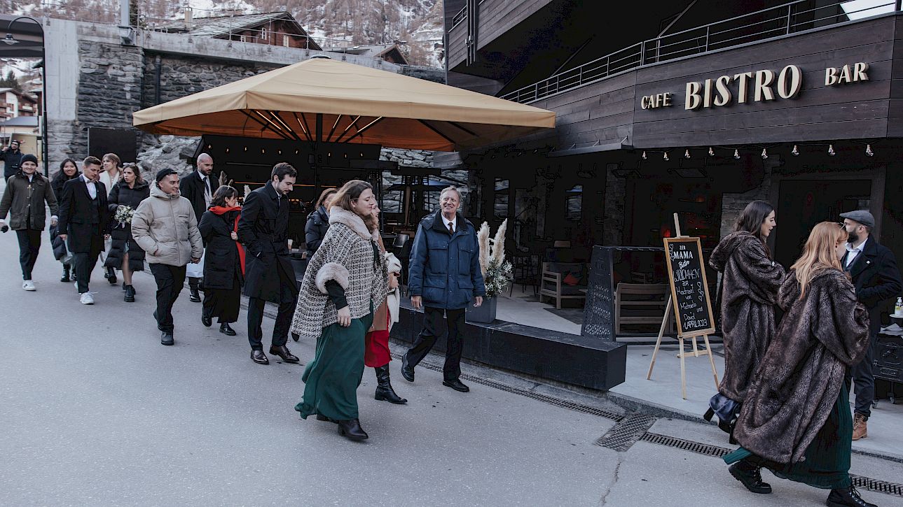 Un groupe de personnes passe devant un café-bistro par temps froid, certains portent des manteaux chauds.