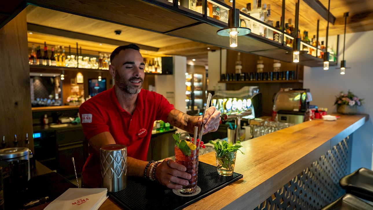Barman prépare un cocktail coloré au comptoir en bois d'un bar accueillant.