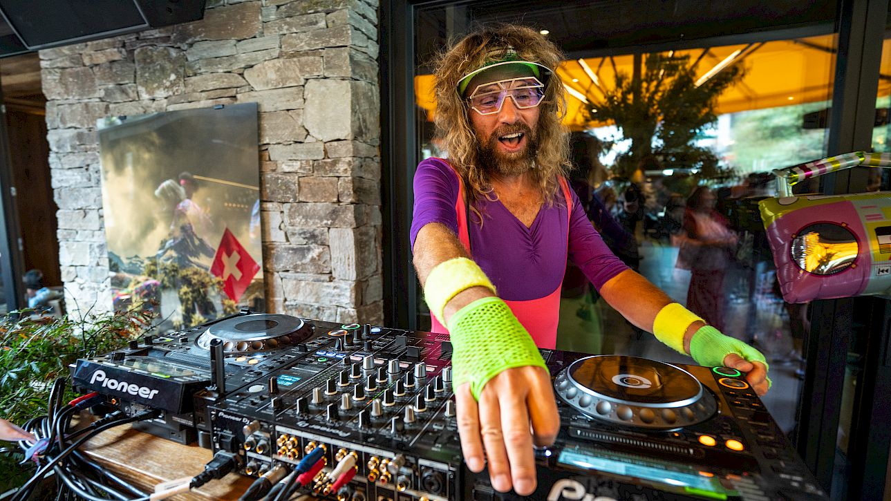 DJ en tenue rétro colorée jouant de la musique en plein air, drapeau suisse en arrière-plan.