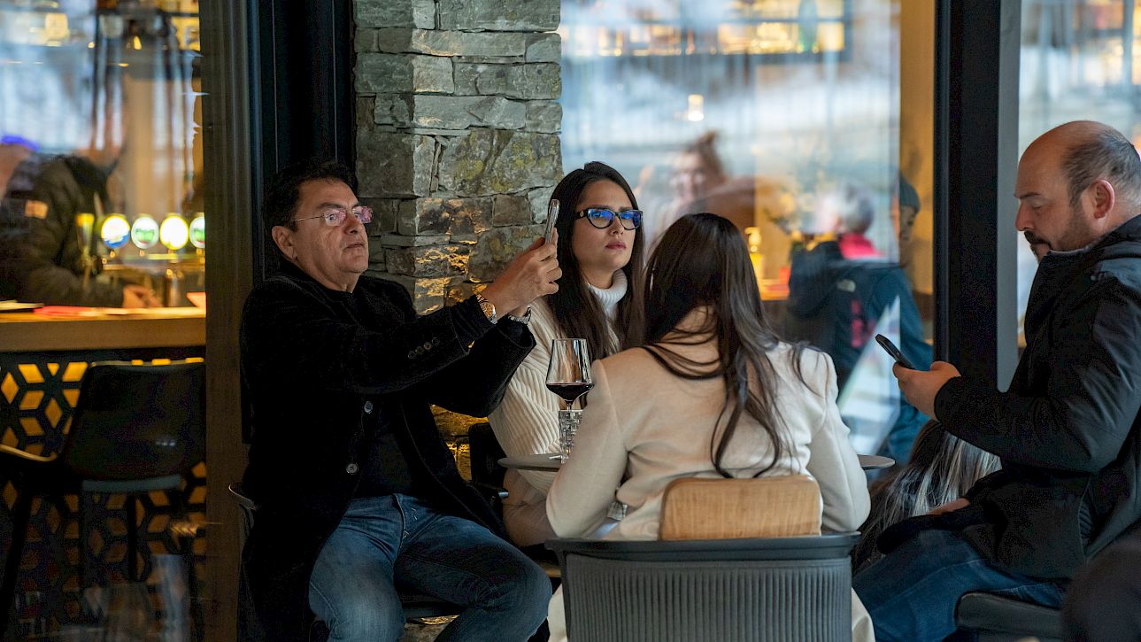 Four people sitting in a café. A man holds a drink while two others look at their phones.