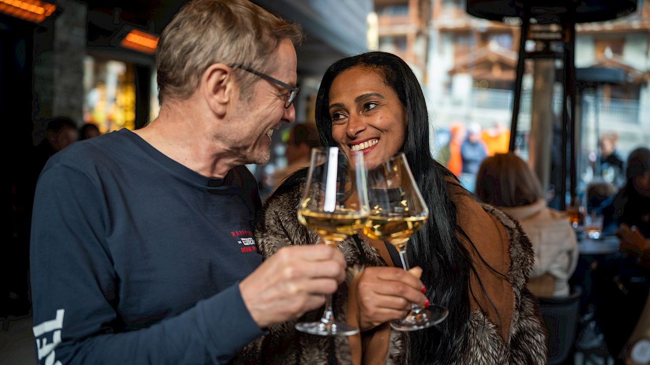 A man and a woman clink wine glasses in a cozy restaurant, smiling