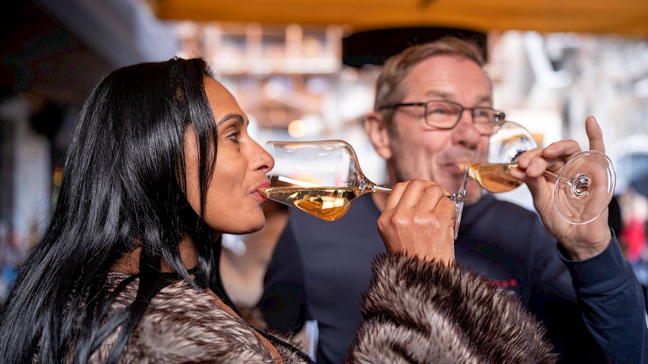 Two people in winter attire enjoying a glass of white wine outdoors.