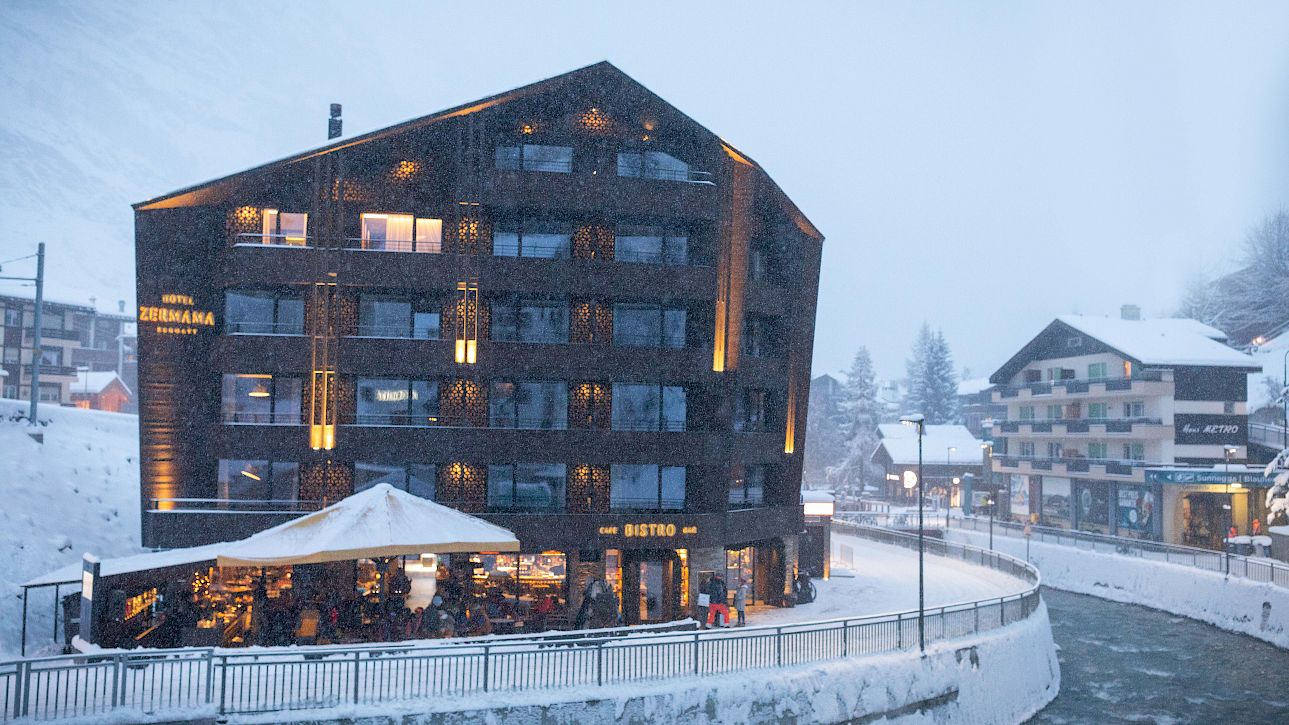 Modern hotel and bistro in snowy Alpine village during snowfall.