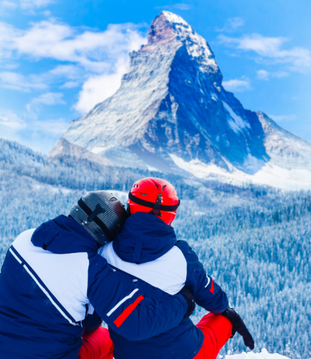 Zwei Skifahrer sitzen vor dem Matterhorn, umgeben von schneebedeckten Bergen und blauem Himmel.