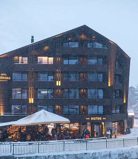 Ein modernes, beleuchtetes Hotel in den verschneiten Bergen, mit einem besuchten Bistro im Erdgeschoss.
