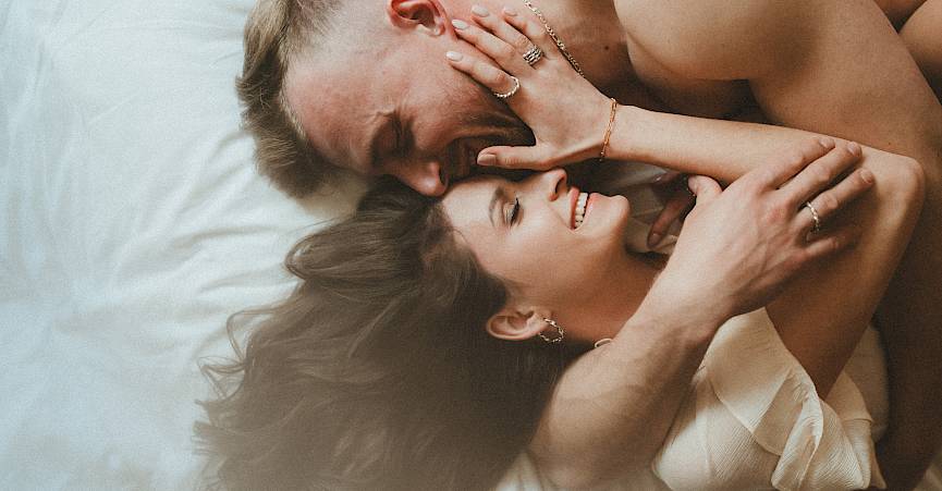 Un couple souriant est allongé étroitement sur le lit, partageant un moment intime.