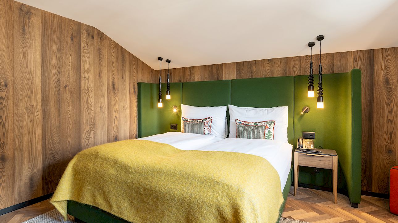 Gemütliches Schlafzimmer mit Holzwand, grünem Kopfteil und gelber Decke auf einem Doppelbett.