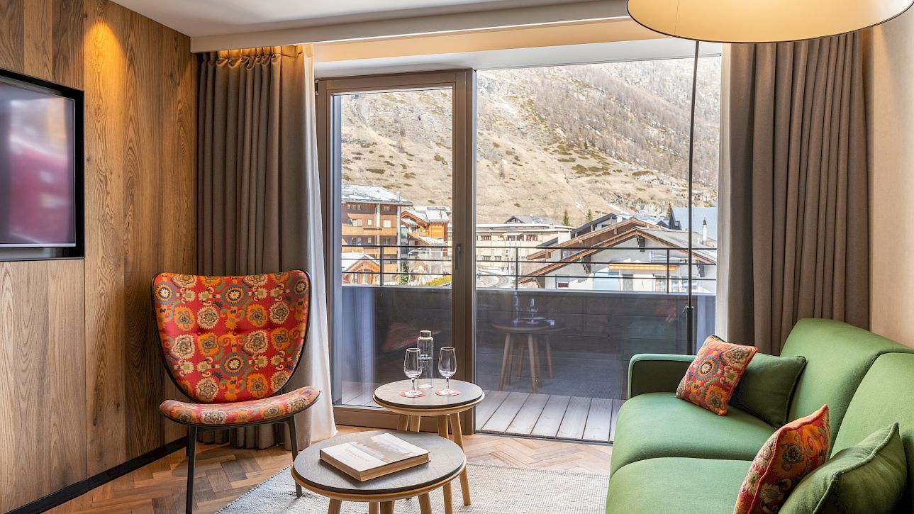 Modernes Wohnzimmer mit grünem Sofa, buntem Sessel und Fenster mit Bergblick.
