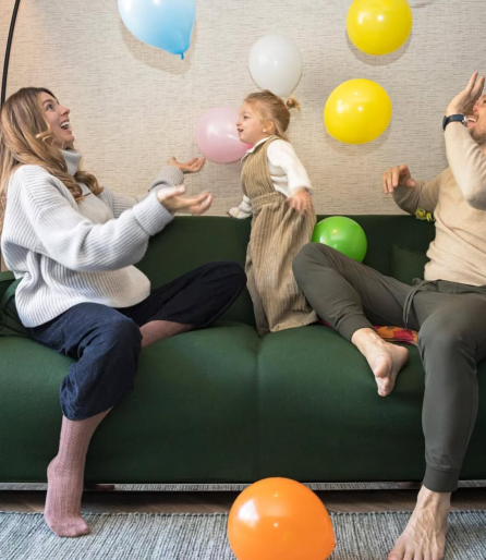 Familie sitzt auf Sofa und spielt fröhlich mit bunten Luftballons.