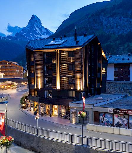 Bâtiment moderne à Zermatt au crépuscule, avec le Cervin en arrière-plan, entouré de paysage alpin.