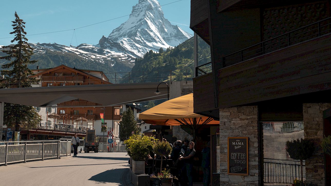 Straßenszene in den Alpen mit dem Matterhorn im Hintergrund, Cafés und Geschäfte entlang der Straße.