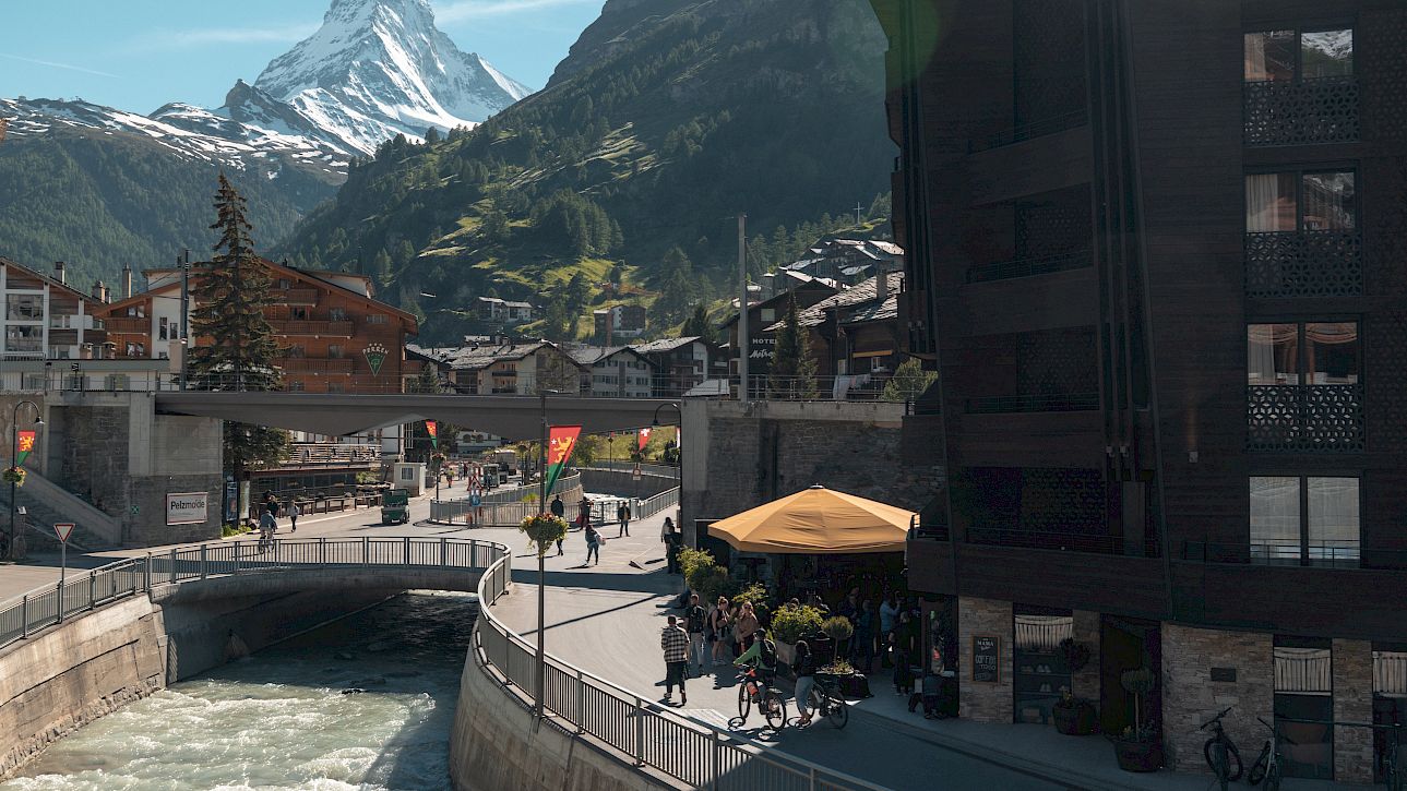 Bergblick auf das Matterhorn, mit einer belebten Straße und einem Fluss in einer malerischen Stadt.
