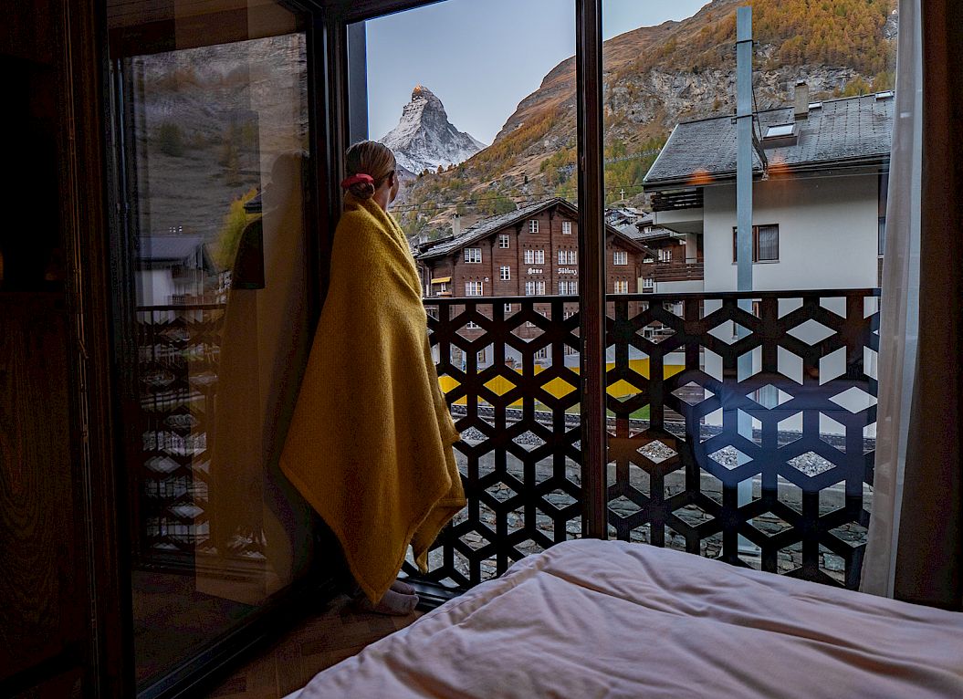 Une personne enveloppée dans une couverture se tient sur un balcon avec vue sur les montagnes.
