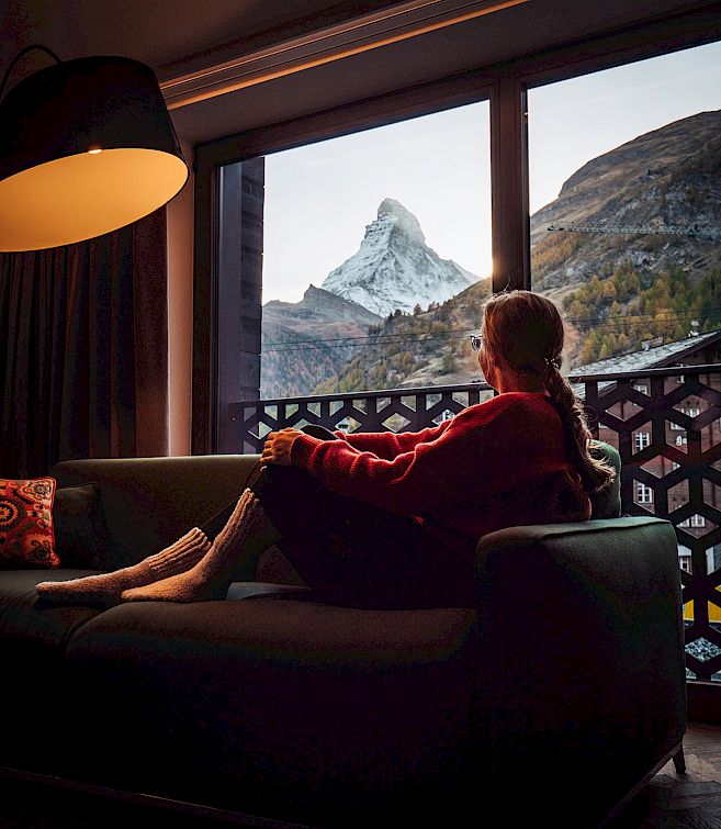 Une personne est assise sur un canapé, regardant par la fenêtre le Cervin au crépuscule.