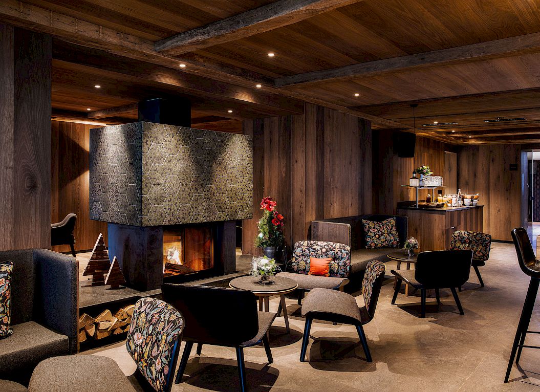 Salon chaleureux avec murs en bois, cheminée centrale, fauteuils confortables et ambiance élégante.