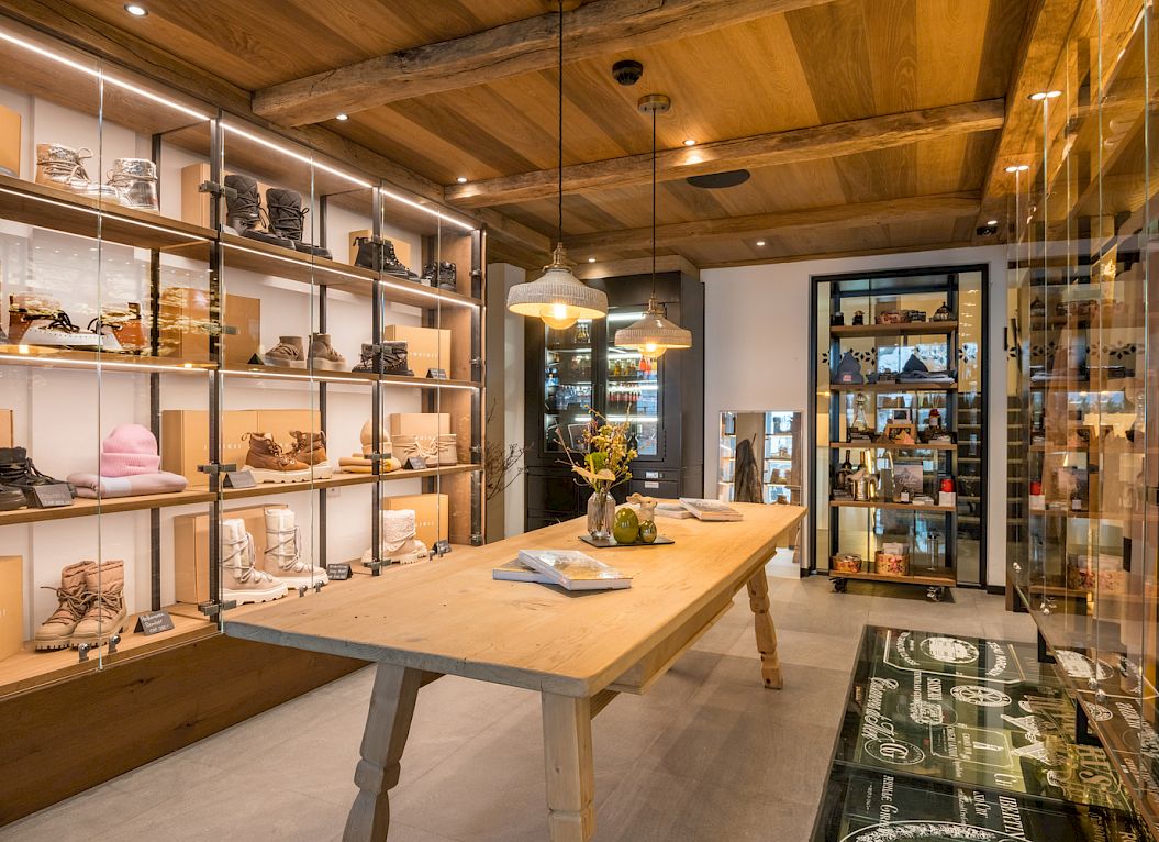 Une boutique chaleureuse avec des meubles en bois et des chaussures sur étagères, éclairée par des suspensions chaleureuses.