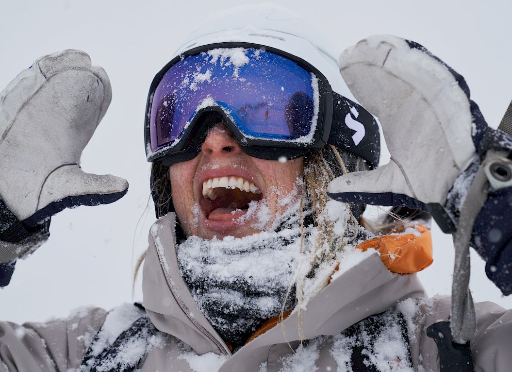Woman in ski goggles and helmet, laughing, covered in snow, enjoying a winter wonderland.