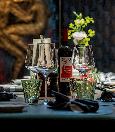 Eleganter Tisch in einem Restaurant, gedeckt mit Weingläsern, Besteck und Dekoration, im Hintergrund Kunstwerk.