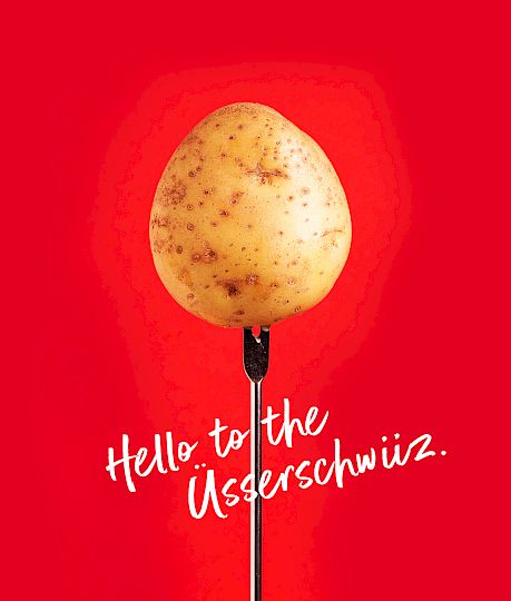 Kartoffel auf einer Gabel vor rotem Hintergrund mit dem Text: "Hello to the Üserschwiiz."