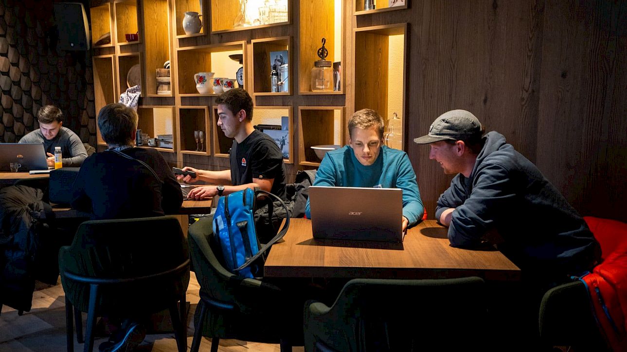 Des personnes travaillent sur des ordinateurs portables dans un café chaleureux avec étagères en bois et lumière douce.