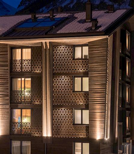 Bâtiment moderne de nuit, avec éléments de façade illuminés et toit enneigé dans une ville.