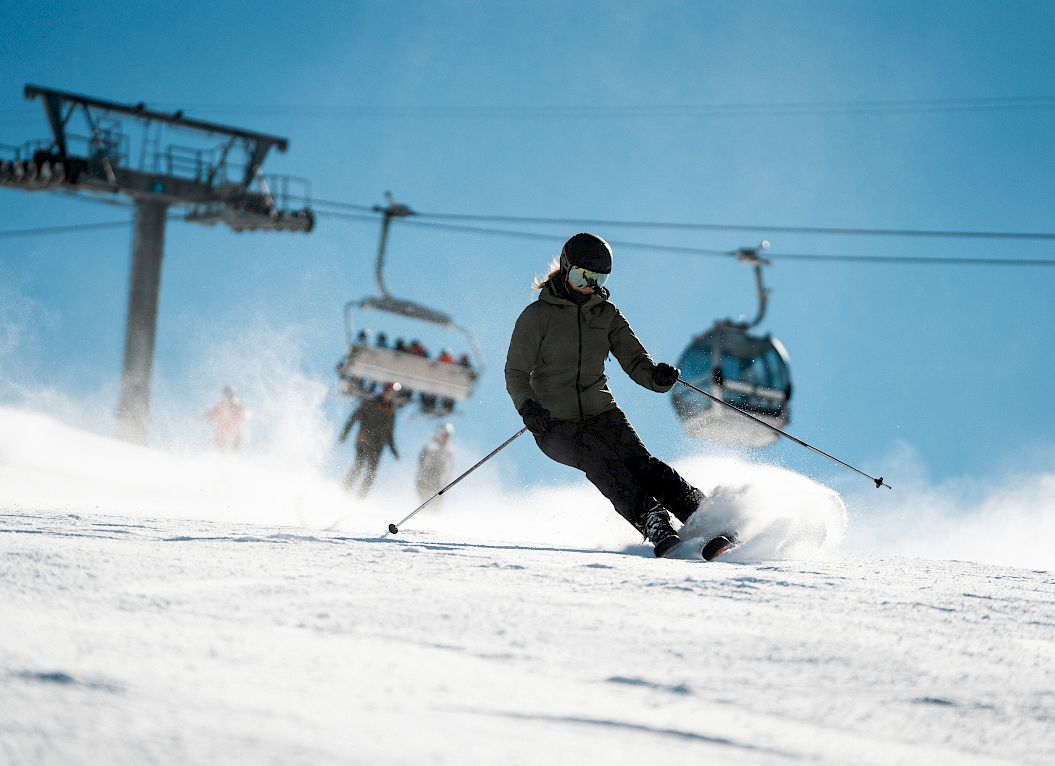 Skier descending a snowy slope in black attire, chairlift visible in the background.