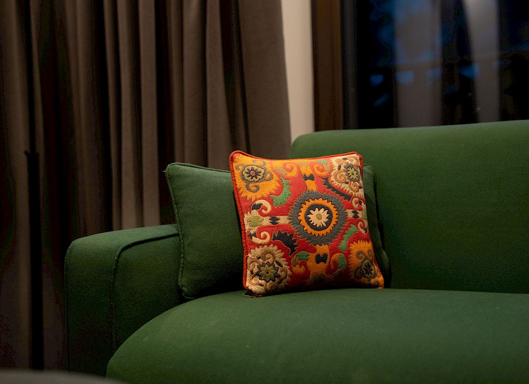 Green sofa with a colorful decorative pillow in a cozy room. Dark curtains in the background.