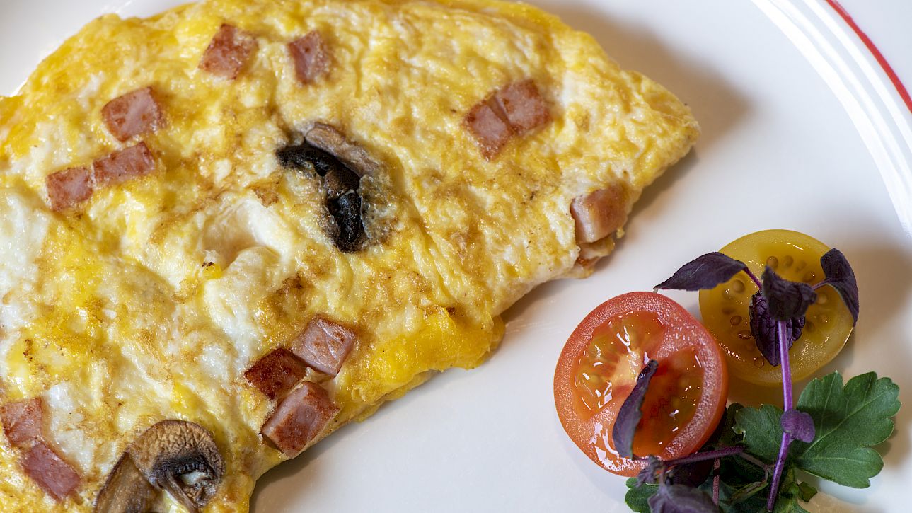 Omelette with mushrooms and ham, served with cherry tomatoes and herbs on a white plate.