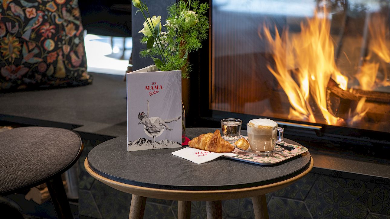 Cozy scene with coffee and pastry on a table, by a roaring fireplace.