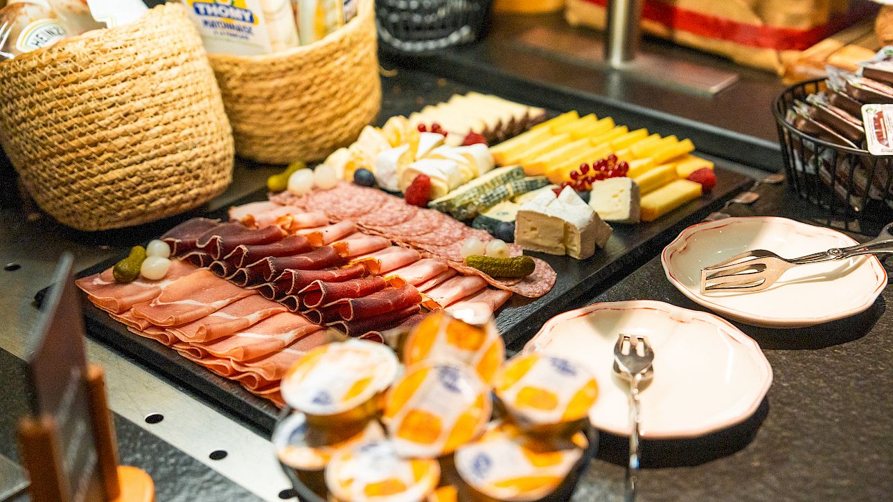 Various cold cuts and cheeses served on a buffet, with bread baskets and small butter portions.