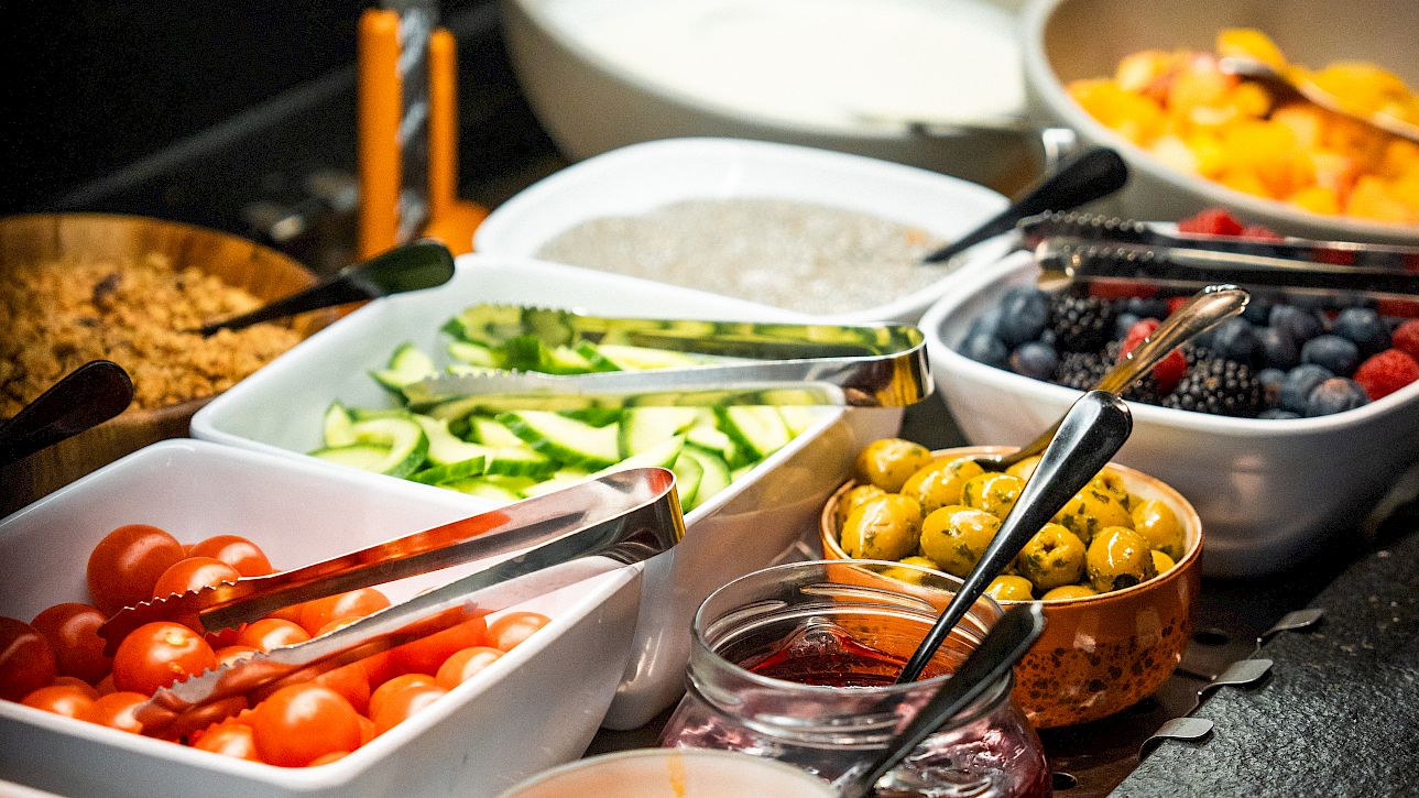 A breakfast buffet with fruits, vegetables, spreads, and cereals arranged in bowls and dishes.