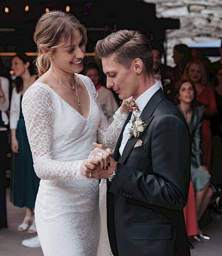 Les mariés dansent intimement lors de leur mariage, entourés d'invités élégamment vêtus.