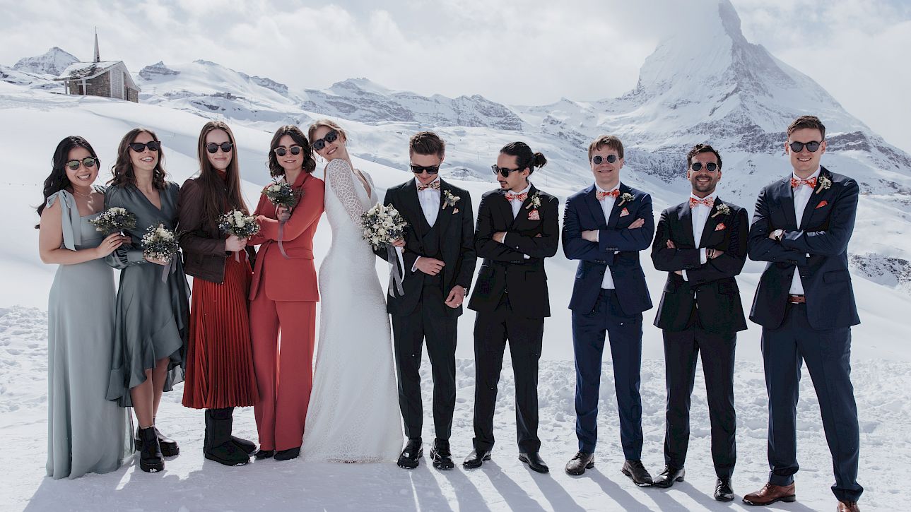 A wedding party poses stylishly in the snow against a picturesque Alpine backdrop featuring the Matterhorn.