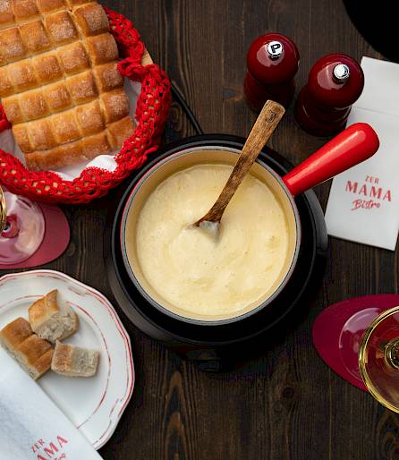 Fondue set on wooden table with bread, two wine glasses, and two red and white napkins.