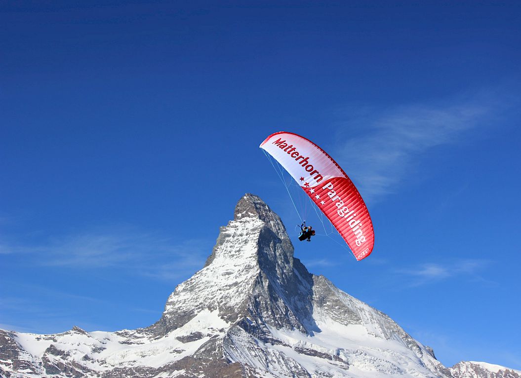 Paraglider soaring in front of the Matterhorn under clear blue sky in the Swiss Alps.
